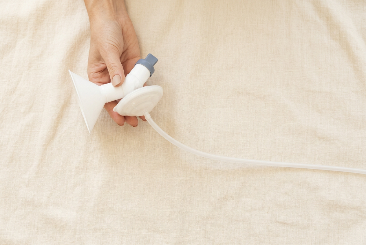 Hand holding the Pump For Joy breast pump connector and flange on warm cream linen
